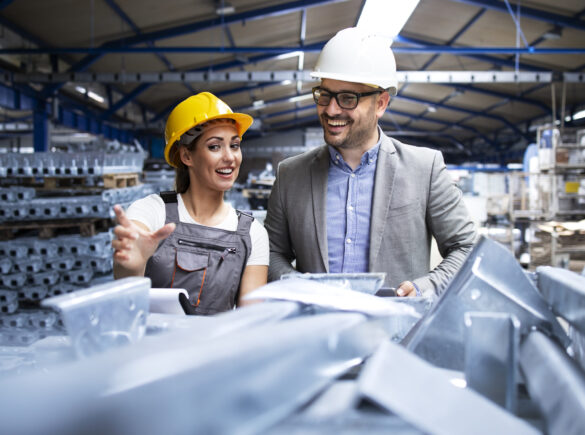 Factory worker wearing hardhat and uniform showing new metal products to the manager supervisor.